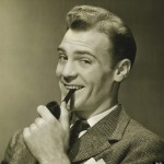 Businessman holding pipe in mouth, smiling, (B&W), portrait